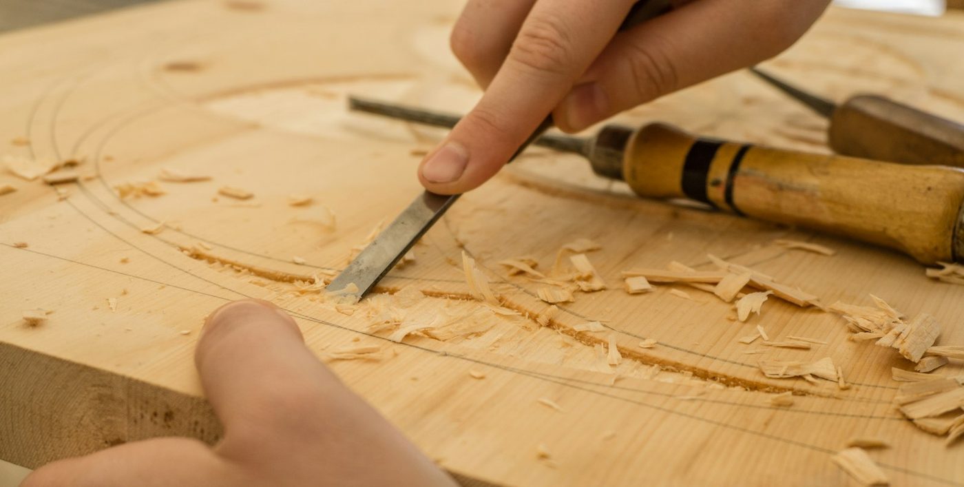 Manos de ebanista trabajando la madera con una gubia